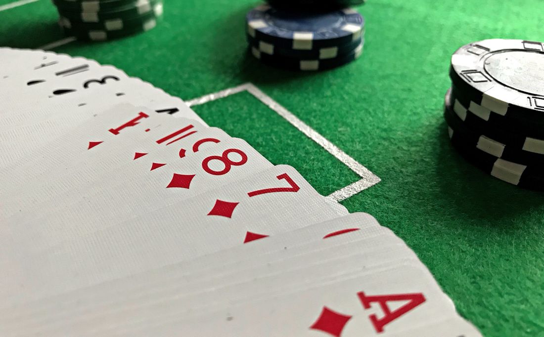 Tumpukan chip poker biru, hijau, dan ungu di atas meja felt